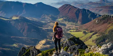 Widok na jesienne pasmo górskie Mała Fatra. Kobieta z plecakiem podziwia panoramę z kamienistego szczytu.