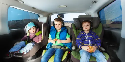 Trzech chłopców w fotelikach samochodowych. Najmłodszy w niebieskiej czapeczce, środkowy w słuchawkach z ciastkiem, a najstarszy trzyma jabłko.