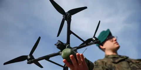 Młody dron wiek. Żołnierz w zielonym beretcie trzyma w dłoniach nowoczesny dron z kamerą i zielonym ładunkiem.