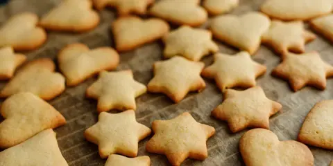 Upieczone ciasteczka z foremek w kształcie gwiazdek i serduszek leżą na papierze do pieczenia.