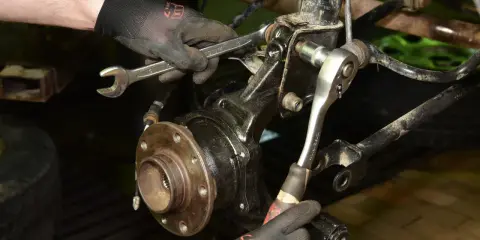 Mechanik w rękawiczkach używa kluczy do wymiany łożyska w piasty koła samochodu.