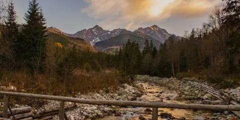 Jesienne Tatry w październiku. Drewniany mostek nad kamienistym potokiem, w tle góry i lasy.