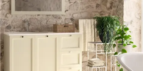 Bagni rustici di campagna con mobile lavabo color crema, cesto in vimini, piante verdi e pareti in pietra grezza.