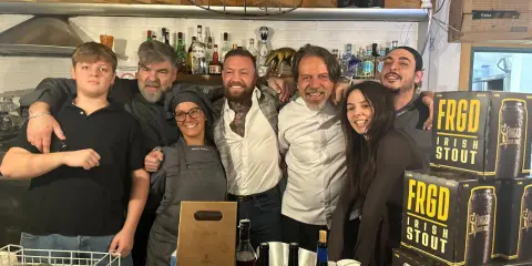 Staff sorridente a Misano Adriatico, con un ragazzo che sembra un gambero sbronzo tra loro. Sul bancone, bottiglie e lattine di "FRGD Irish Stout".