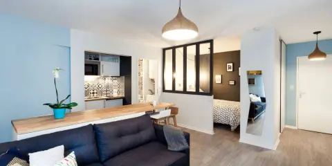 Aménagement studio 30m2 : salon cosy, cuisine moderne, chambre séparée par verrière, et coin repas.