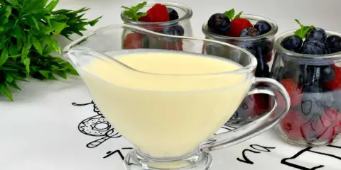 A glass boat filled with smooth, creamy krem angielski, ready to be poured over fresh berries in jars.