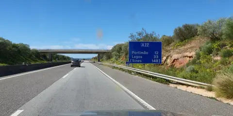 Autobahn A22 in Portugal. Ein Auto fährt auf der rechten Spur, vorbei an einem Schild mit Zielen wie Portimão und Lagos.
