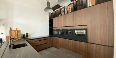Cuisine moderne avec îlot central, plan de travail en marbre noir veiné, meubles en bois, électroménagers intégrés. L'implantation cuisine est pensée pour l'efficacité.