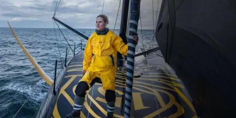 Clarisse Crémer, en tenue de voile jaune vif, se tient fièrement sur le pont d'un voilier, prête à affronter les éléments.