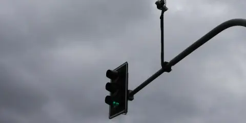 Dwie białe kamery nad światłami sygnalizacji świetlnej, z zielonym światłem.