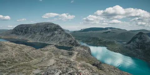 Piękny krajobraz Norwegii, gdzie nie robić nic, tylko podziwiać. Grupa turystów wędruje po skalistym szlaku nad turkusowym jeziorem.