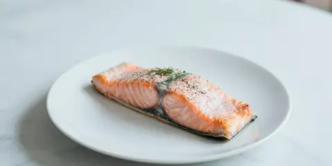 Soczysty łosoś z airfryer, doprawiony pieprzem i świeżym koperkiem, prezentuje się apetycznie na białym talerzu.