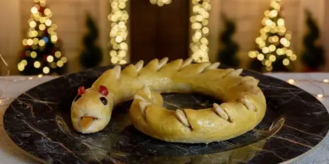 Dolci tipici Perugia: un serpente di pasta frolla dorata, con occhi rossi e lingua arancione, adagiato su un piatto scuro.