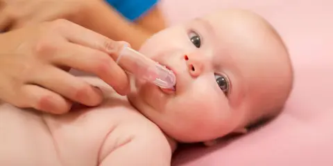 Delikatne czyszczenie ząbków niemowlaka specjalną nakładką na palec. Pokazuje, jak myć zęby niemowlakowi.