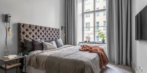 Sovrum med en stor säng, en taklampa och en **gardin på ena sidan av fönstret**.