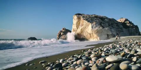 Kamienista plaża na wyspie Afrodyty, gdzie fale rozbijają się o skaliste klify.