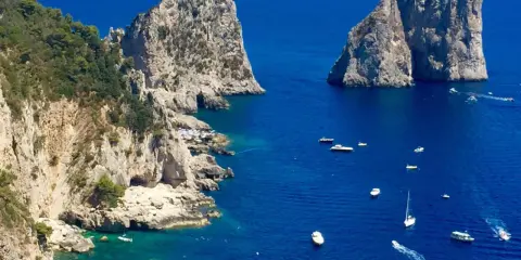 Faraglioni di Capri, tra le più belle isole di Napoli da visitare. Barche navigano nel mare blu intenso.