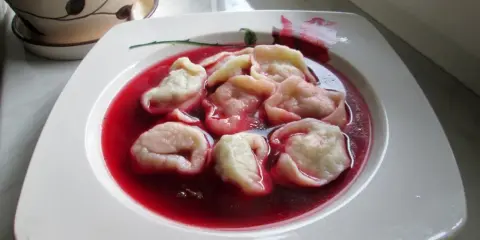 Pyszne uszka z mięsem pływają w czerwonym barszczu na białym talerzu.