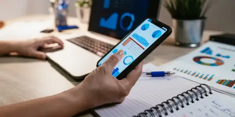 Una gestora de fondos revisa gráficos financieros en su móvil y portátil, analizando datos para tomar decisiones estratégicas.