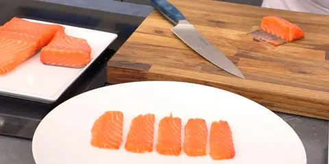 Filetes de salmón marinado listos para servir. Un cuchillo y una tabla de cortar de madera sugieren preparación.