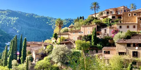 Malerische Häuser mit Zypressen und Palmen, ein grüner Berghang im Hintergrund. Ein friedlicher Anblick von Mallorca im Dezember.