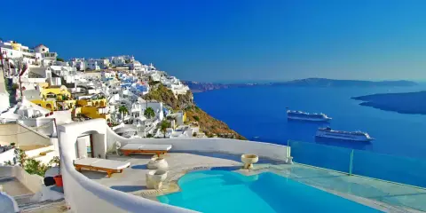 Vista mozzafiato di Santorini con case bianche a picco sul mare blu intenso. Due navi da crociera all'orizzonte, un invito a scoprire crociere a prezzi stracciati.