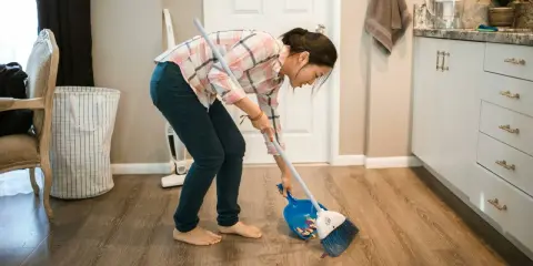 Mujer barriendo el suelo con escoba y recogedor, aplicando trucos de limpieza para mantener el hogar impecable.