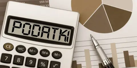 Kalkulator z napisem "PODATKI" obok wykresów i długopisu. Obliczenia podatku od sprzedaży działki.
