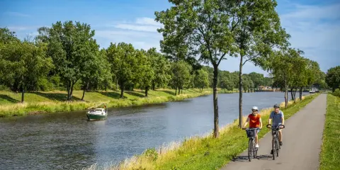 Zwei Radfahrer genießen eine Tour auf dem Dortmund-Ems-Kanal-Radweg. Ein kleines Boot fährt auf dem Wasser.