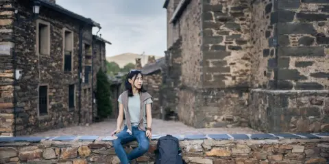 Junge Frau sitzt auf Steinmauer in historischem Dorf in Guadalajara, Spanien.