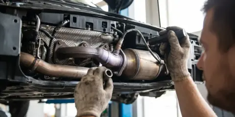 Mechanik w rękawiczkach wymienia element układu wydechowego w samochodzie z instalacją p0420 LPG.