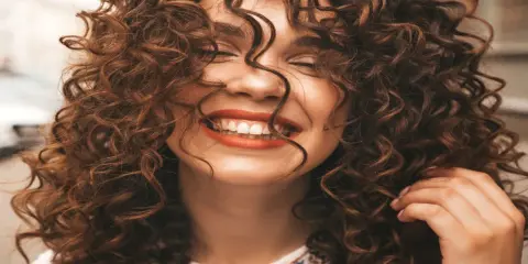 Mujer sonriendo con unos cortes de pelo rizado espectaculares, su cabello castaño cae en cascada alrededor de su rostro.