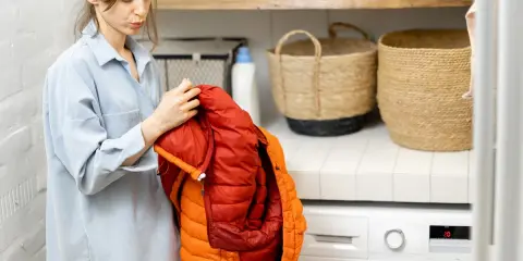 Mujer revisa un anorak naranja y rojo, preparándose para saber como lavar un anorak en la lavadora.