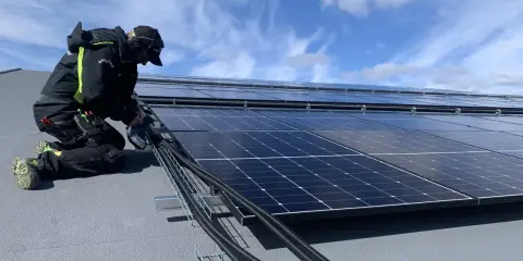 Installatör arbetar med solpaneler, drar kablar. Olika batteri storlekar kan behövas för att optimera energilagringen.