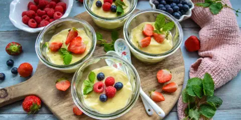 Vier Gläser mit selbstgemachtem Pudding, garniert mit frischen Beeren und Minze. Ein Genuss für Augen und Gaumen!