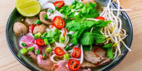 Un bol de soupe pho savoureux avec du bœuf, des boulettes, des nouilles, des herbes fraîches, des piments et un quartier de citron vert.
