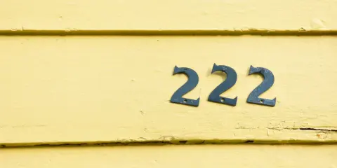 Niebieskie cyfry 222 na żółtej, drewnianej ścianie. Liczba 222 ma dla mnie szczególne znaczenie.