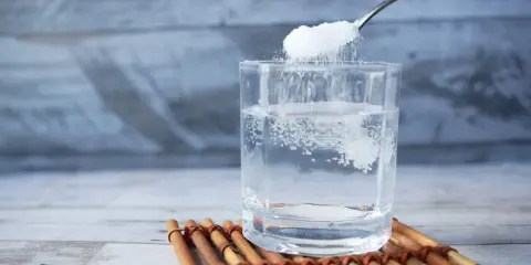 Salz und Zucker werden in ein Glas Wasser gegeben, um Elektrolyte selber machen.