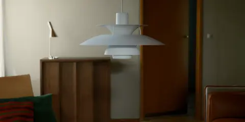 En ikonisk PH-lampa från Poul Henningsen hänger över ett vardagsrum med en läderfåtölj och en träbyrå.