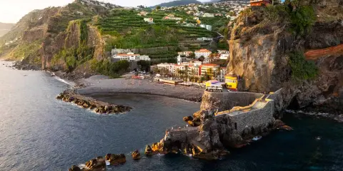 Ponta do Sol, Madeira: malerische Küstenstadt mit terrassierten Bananenplantagen, einem Kiesstrand und einer beeindruckenden Felsformation mit einem steinernen Aussichtsweg.