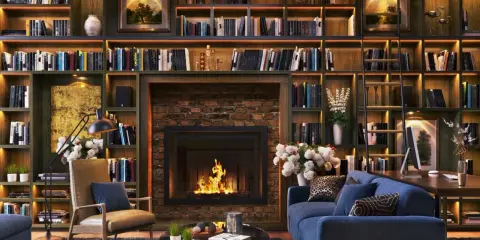 Przytulna biblioteczka w salonie z kominkiem, wygodną kanapą i fotelem.