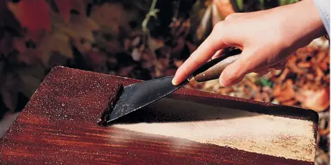 Main d'une personne utilisant un grattoir pour décaper peinture sur bois avec bicarbonate.