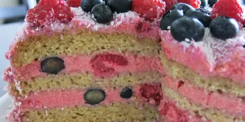 Pyszny wegański krem do tortu z malinami i borówkami, ozdobiony wiórkami kokosowymi. Idealny na letnie przyjęcie.