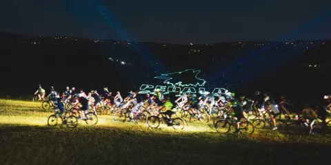 Ciclisti nella notte, illuminati da laser che formano il logo "Pedala coi Lupi". Un'avventura notturna su due ruote.