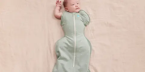 Un neonato dorme sereno, avvolto in una fascia che lo culla dolcemente.