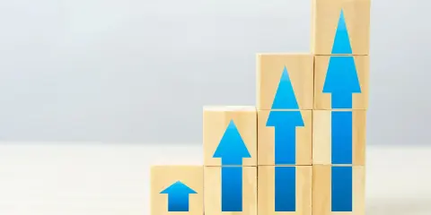 Blocchi di legno impilati a gradoni, con frecce blu che indicano crescita, simboleggiano il superamento dello skills gap e il progresso.