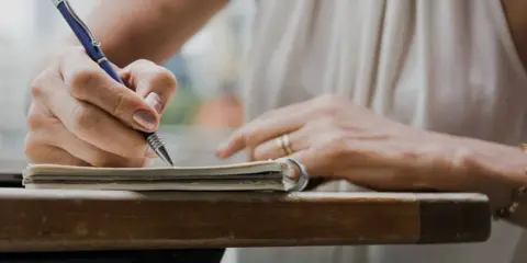 Dłoń pisze długopisem w notatniku, ucząc się, jak napisać artykuł.