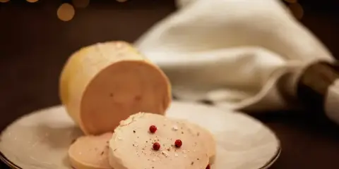 Tranche de foie gras, une des spécialités culinaires Dordogne, assaisonnée de poivre et de baies roses sur une assiette blanche.