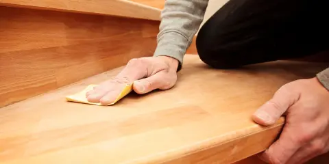 Mann schleift mit Sandpapier eine Holztreppe, um sie zu renovieren.