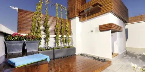 Jardineras de exterior con flores rojas y enredaderas. Un espacio moderno con ducha y terraza de madera.